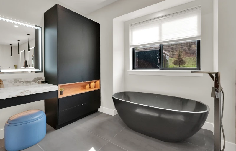 Modern bathroom with black freestanding tub, black cabinetry, marble vanity, and backlit mirror.