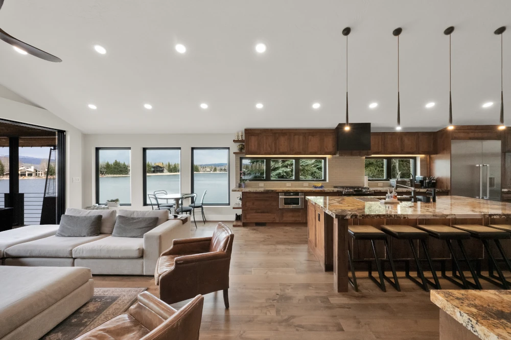 Whole home remodel with open-concept living room and kitchen, wood cabinetry, granite waterfall island with bar seating, and picture windows overlooking a lake