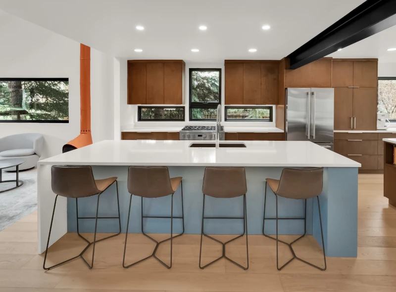 Kitchen remodel with a large white quartz waterfall island, leather bar stools, walnut cabinetry, stainless steel appliances, and exposed black steel beam