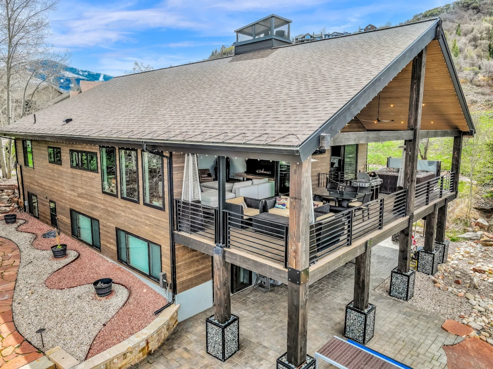 Aerial view of a remodeled mountain home with cedar siding, elevated covered deck, cable railing, and timber post supports