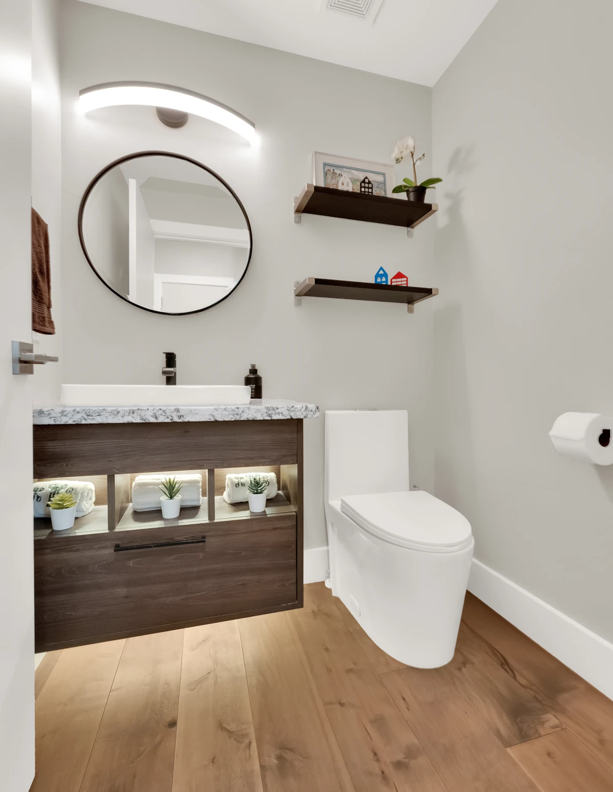 Powder room remodel with floating wood vanity, vessel sink, and round black mirror