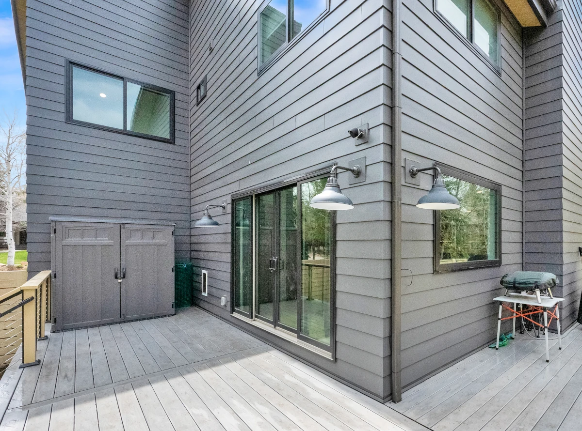 Gray lap siding on a two-story home exterior with black-framed windows, sliding glass doors, barn-style wall sconces, and a gray composite deck