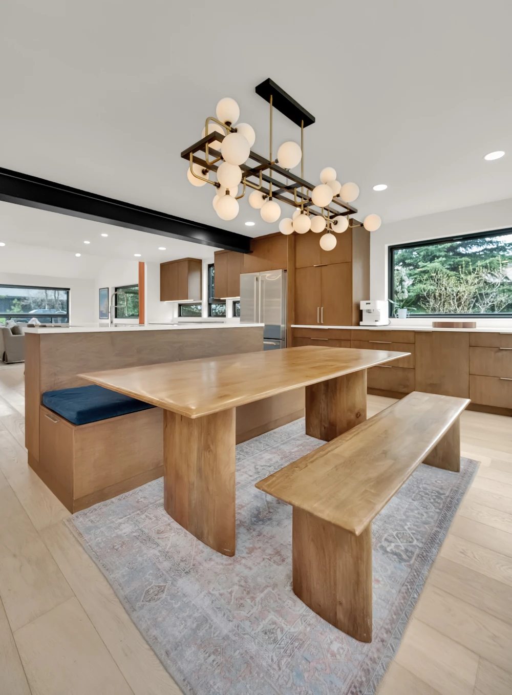 Open-concept kitchen remodel with wood cabinetry, built-in banquette seating, live-edge dining table and bench, and a globe cluster chandelier