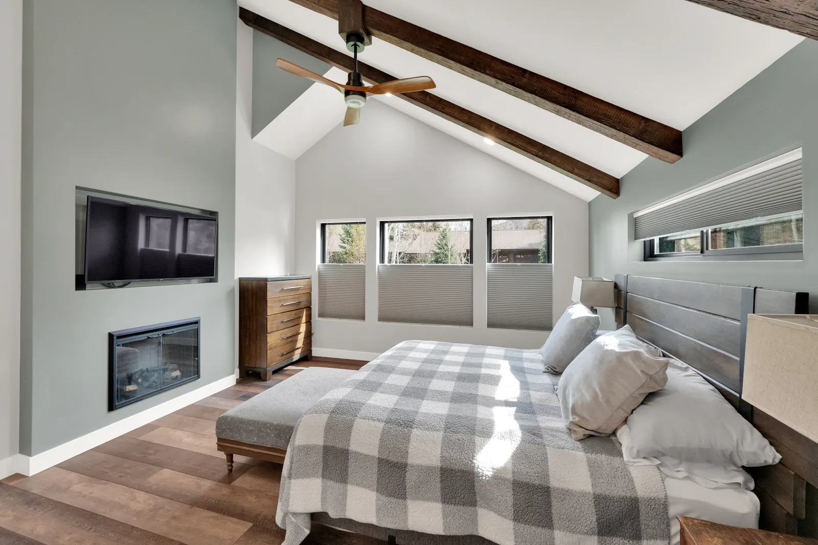 Bedroom home addition featuring cathedral ceiling with rustic beams, wall-mounted TV above fireplace, and wide-plank wood flooring