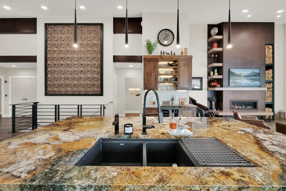 Kitchen island with granite countertop, double basin sink, and pendant lighting overlooking living room