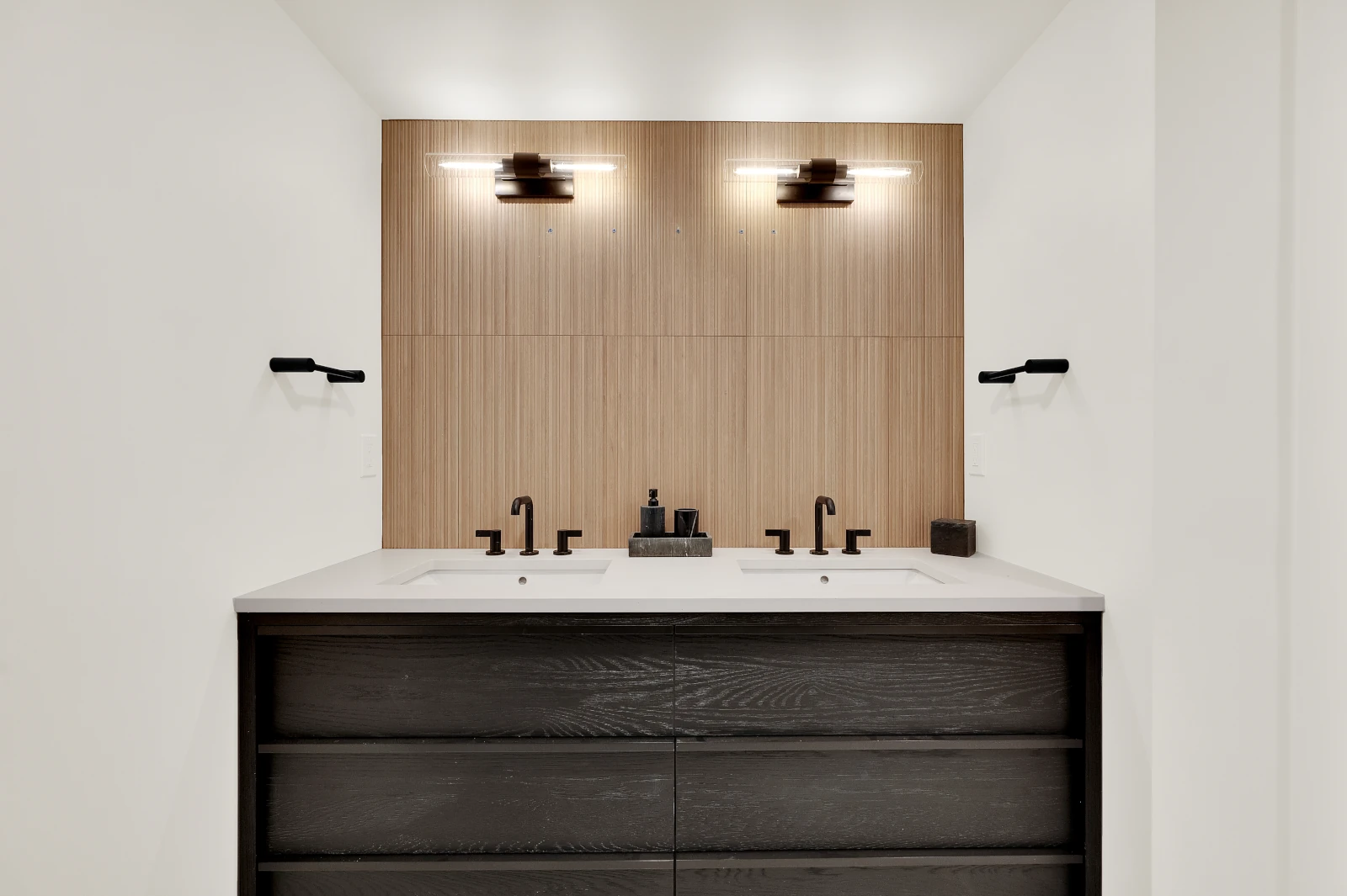Double vanity remodel with black oak cabinetry, white quartz countertop, fluted white oak backsplash, and matte black fixtures