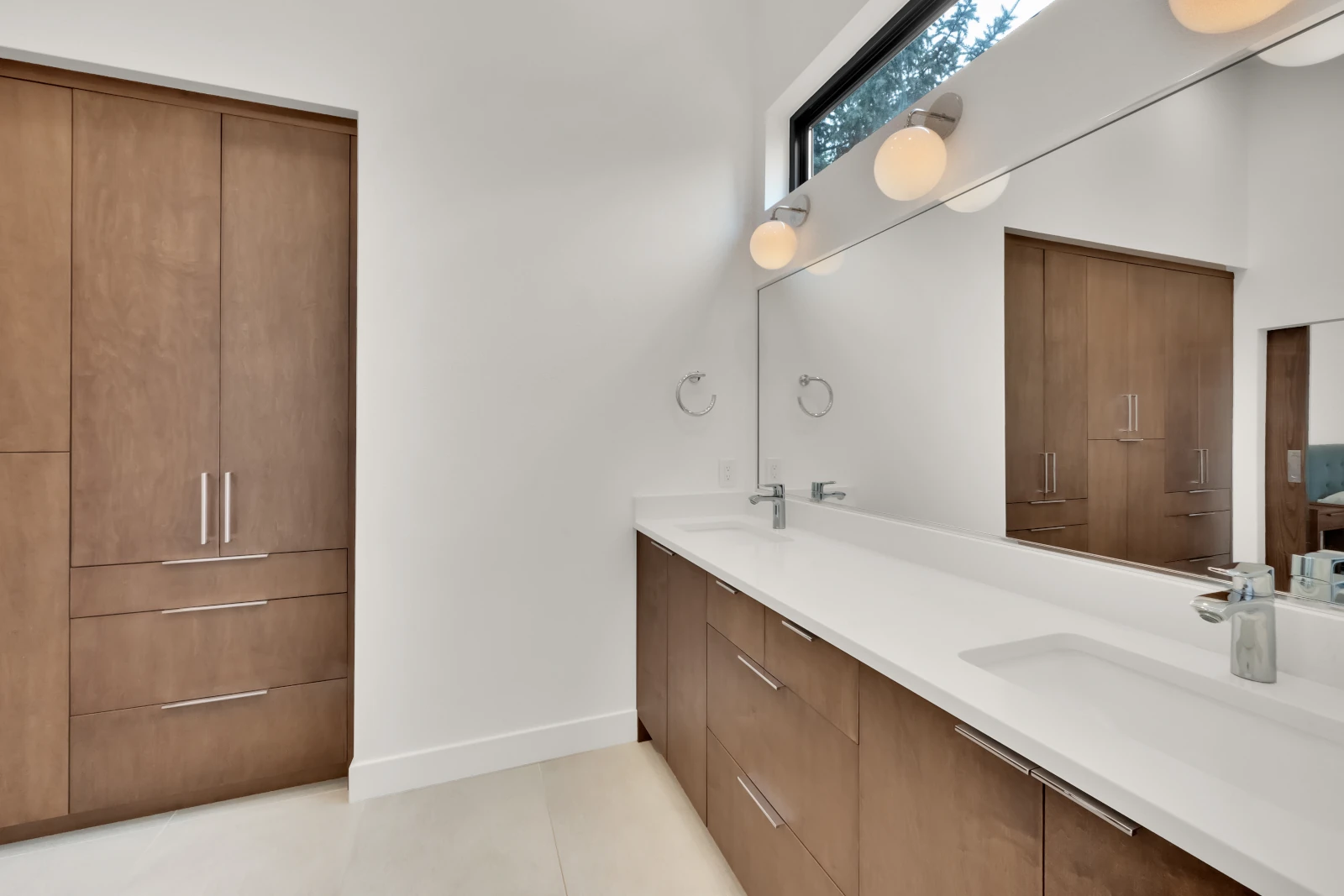 Modern bathroom with floating walnut double vanity, white quartz countertop, full-width mirror, and built-in linen cabinet