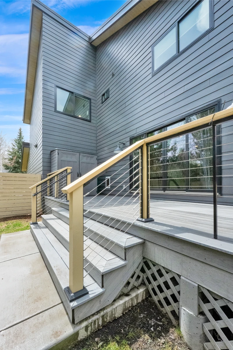 Composite deck stairs with cable railing beside gray lap siding