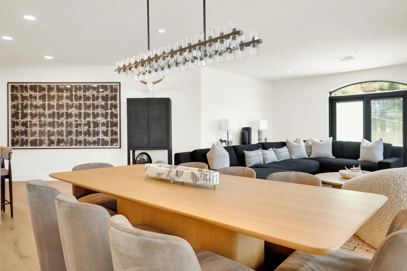 Open dining and living area with white oak table and linear glass chandelier