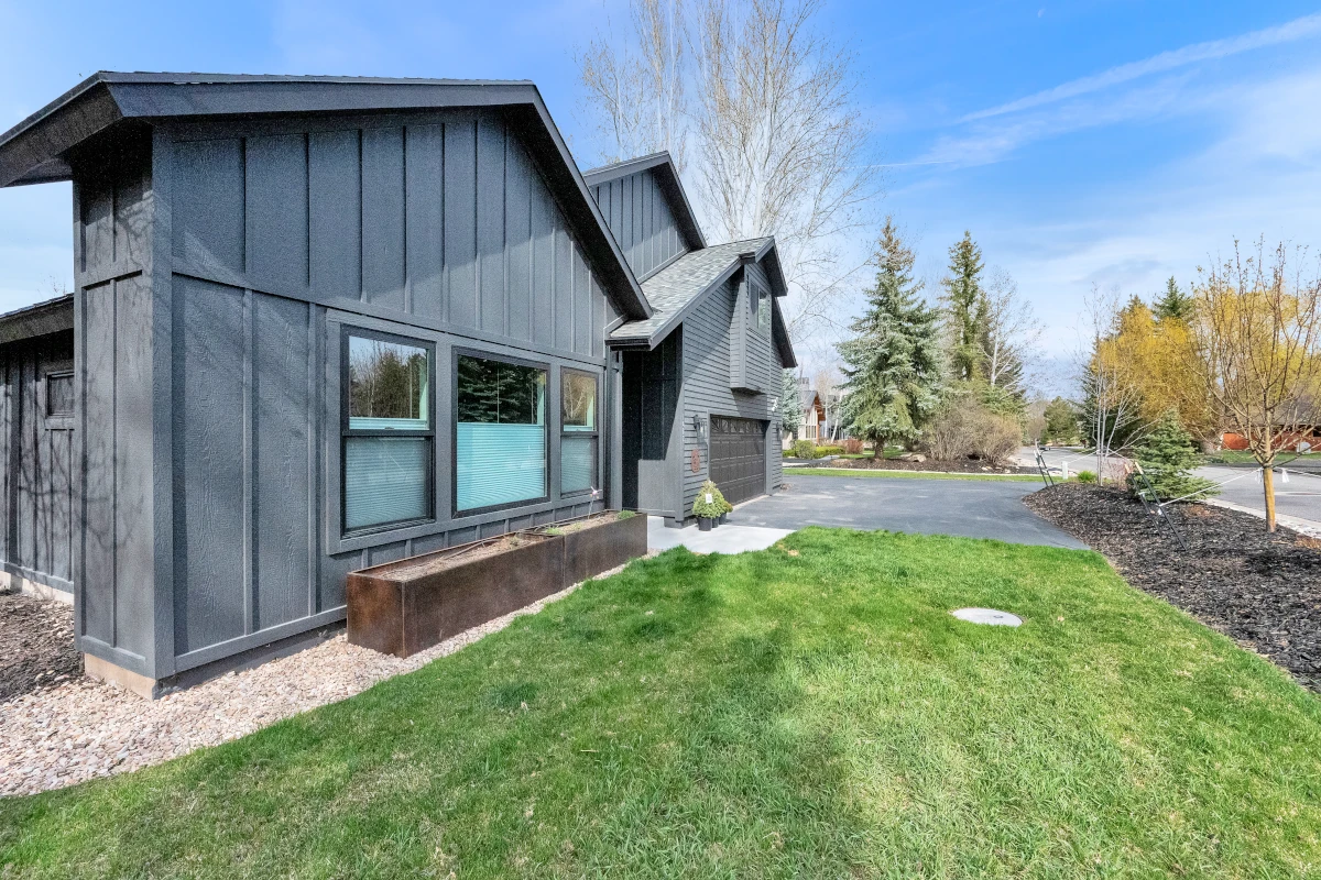 Modern farmhouse exterior with dark board-and-batten siding, metal roof accent, and corten steel planter