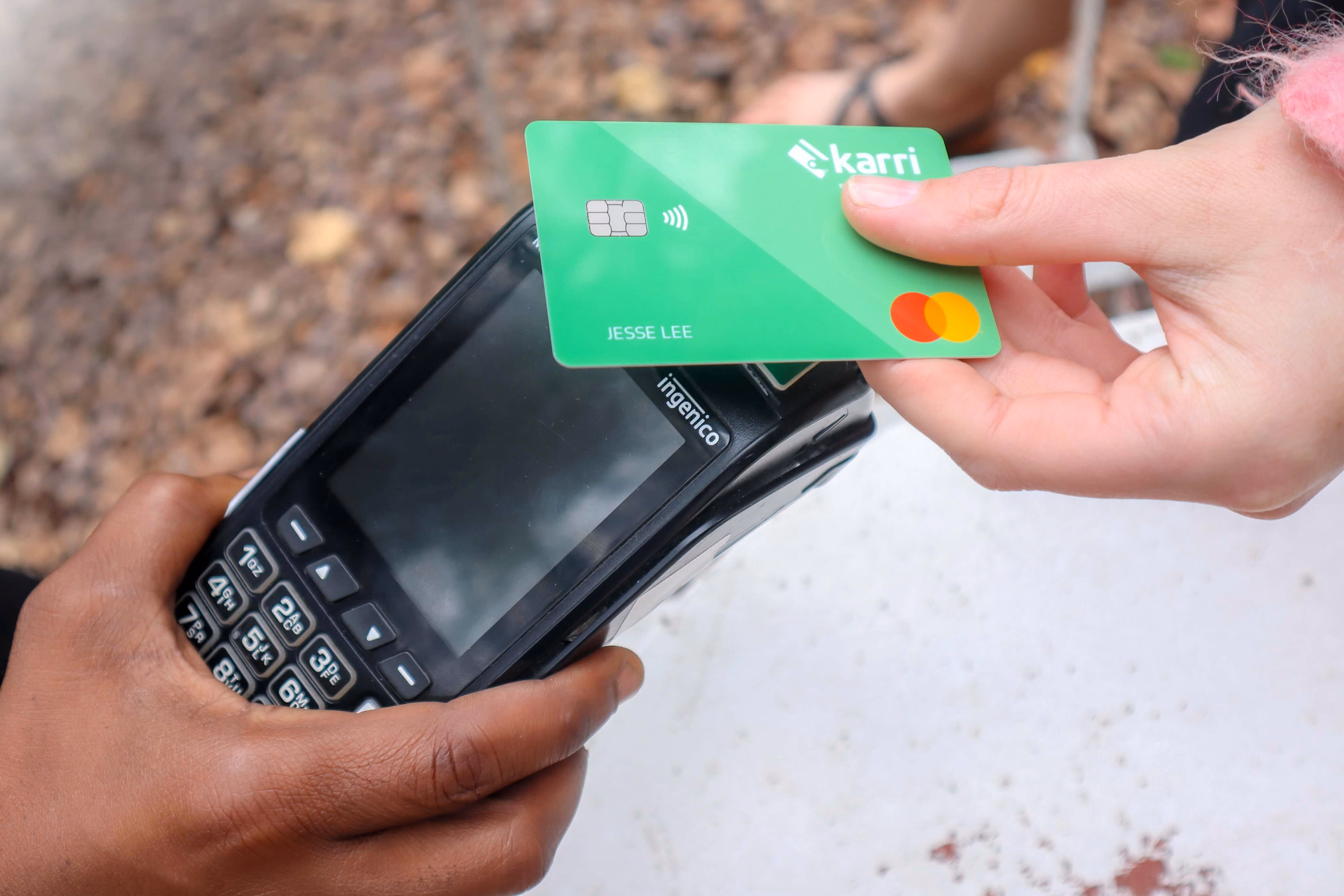 Hand holding a green contactless payment card over a black Ingenico card reader held by another hand.