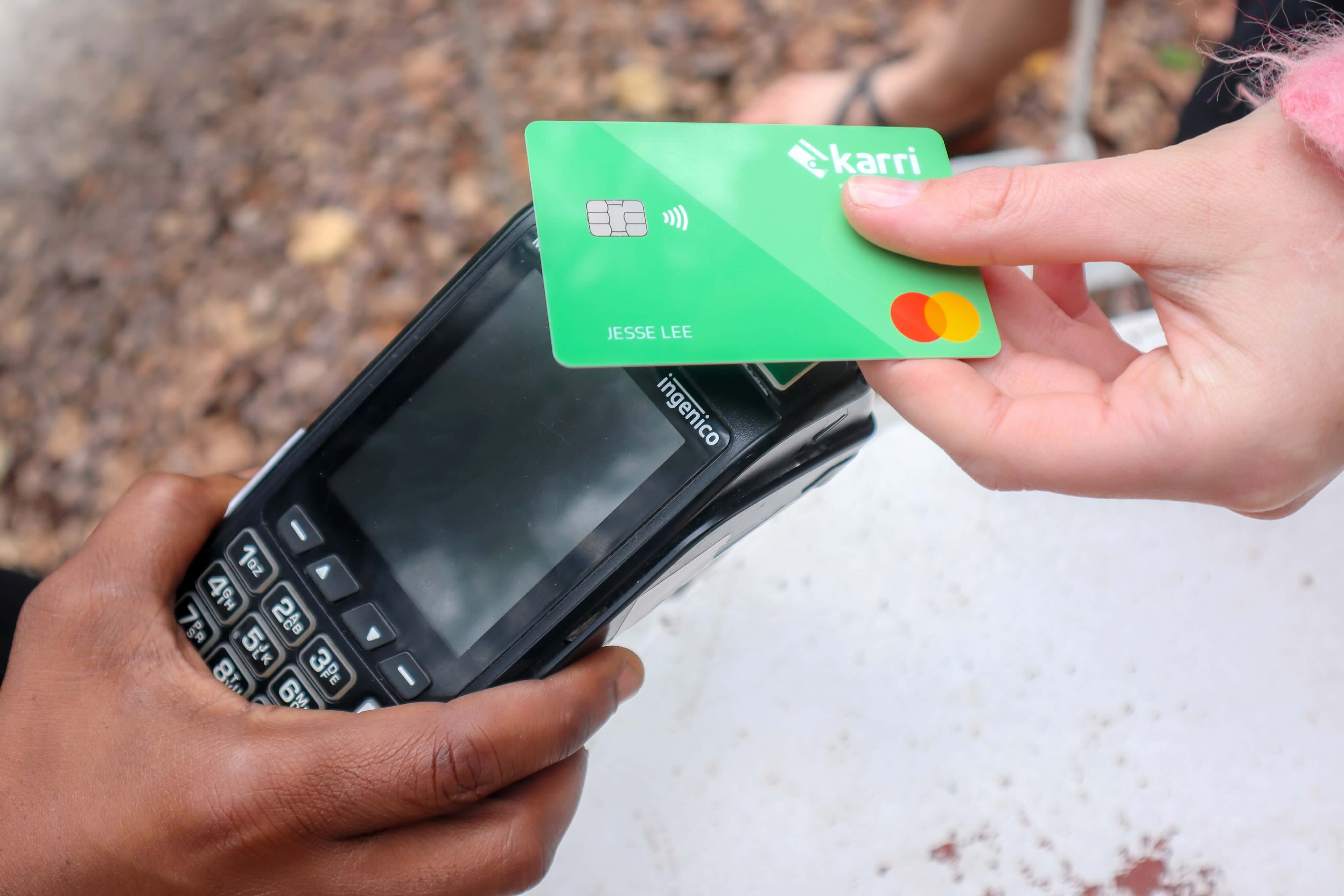 Hand holding a green contactless payment card over a black Ingenico card reader held by another hand.