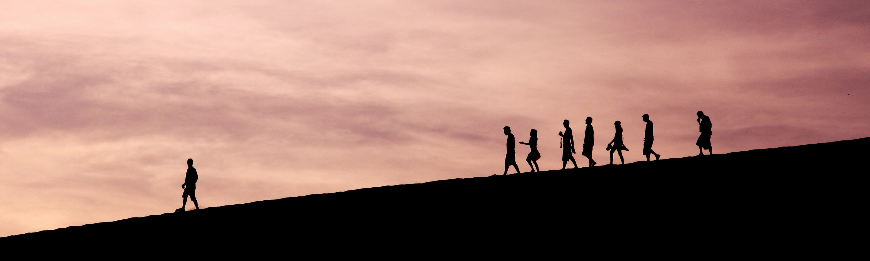 silhouette of a group of people walking on a hill against a sunset.