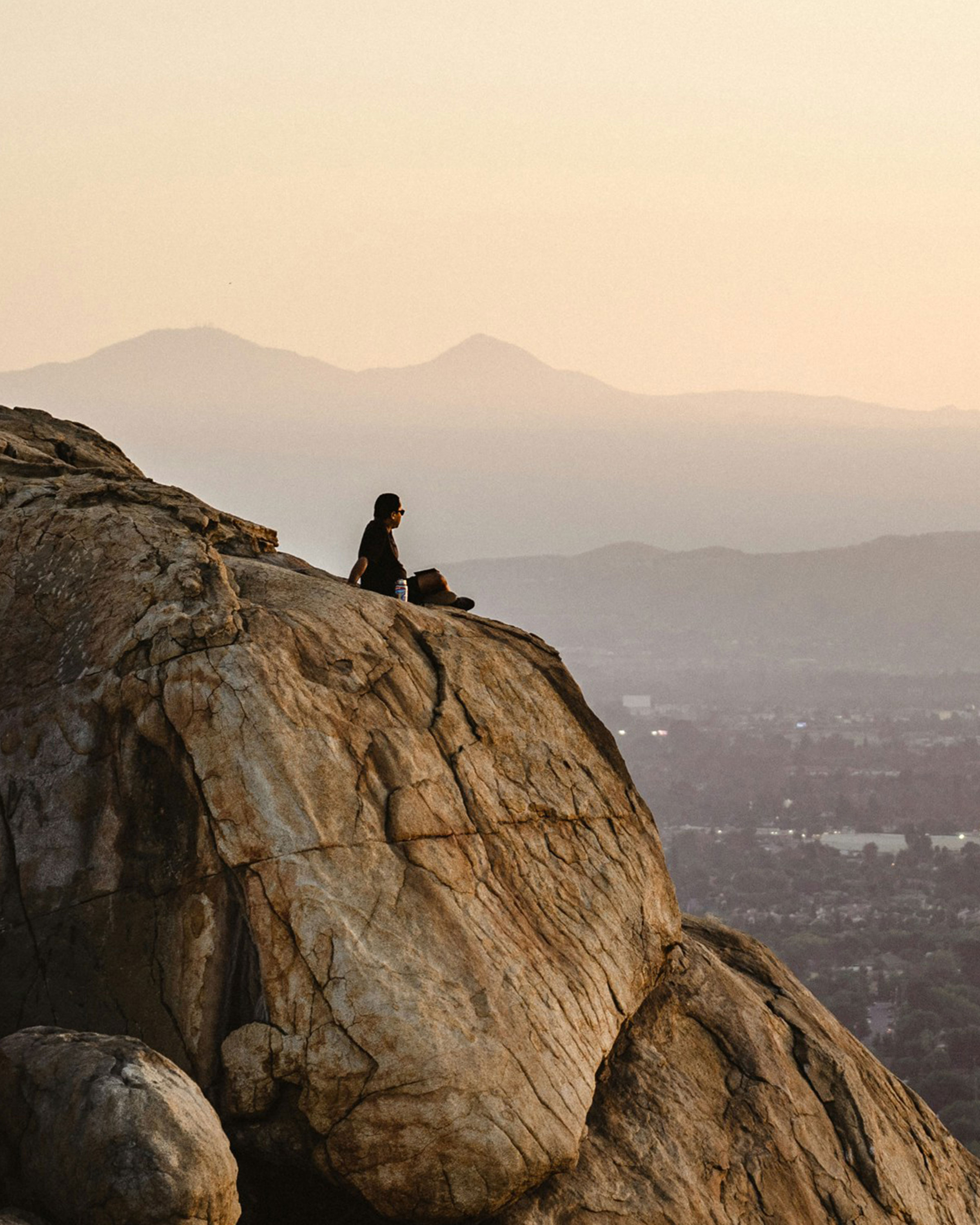 Person sitting on a mountaintop overlooking the city.