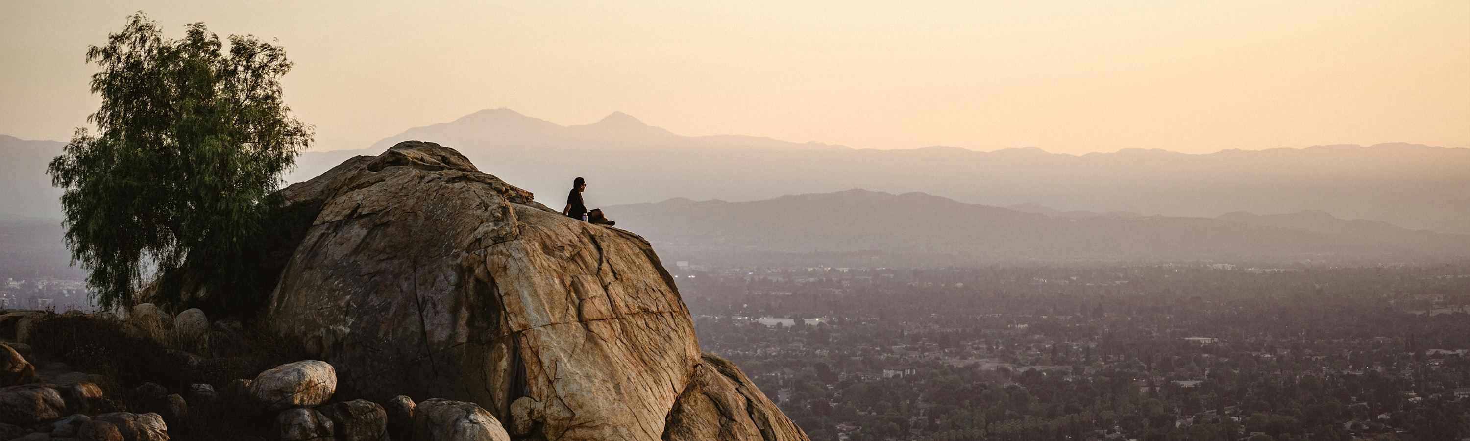 Person sitting on a mountaintop overlooking the city.