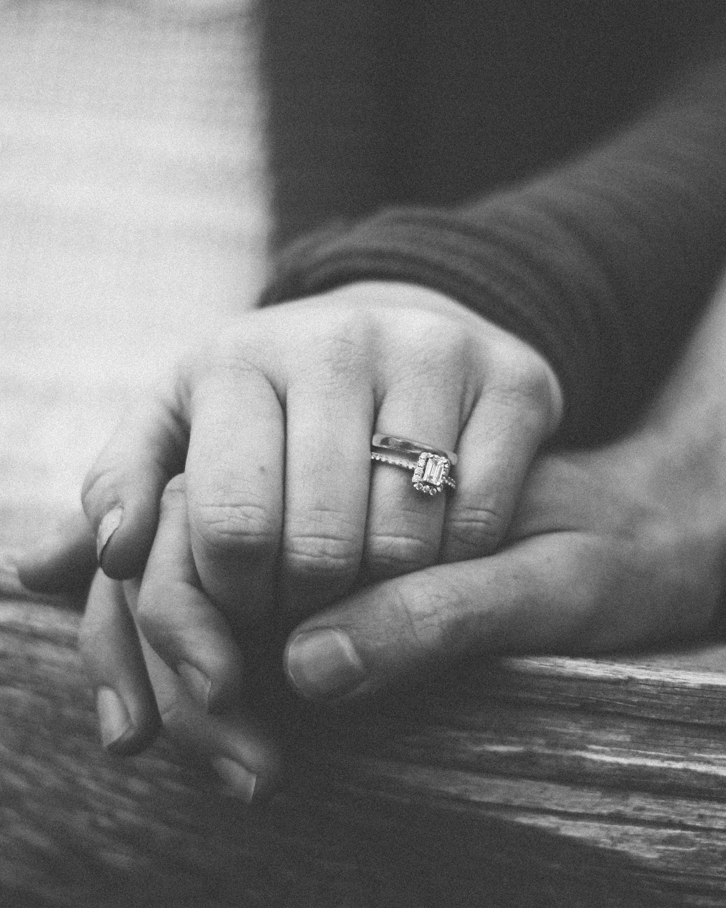 Closeup of a woman's hand holding a man's hand with a wedding ring on her finger.