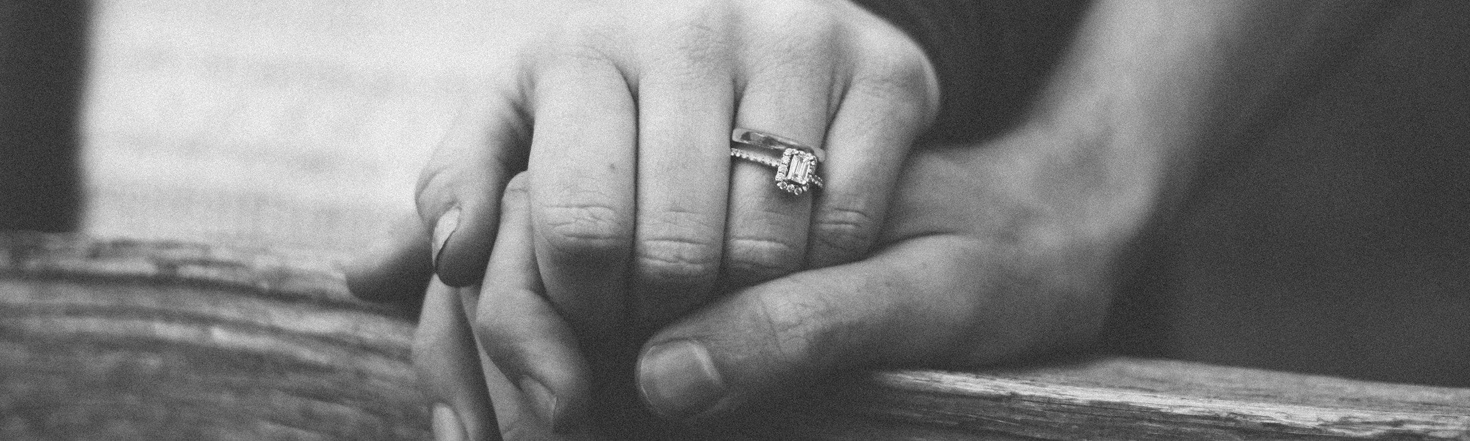 Closeup of a woman's hand holding a man's hand with a wedding ring on her finger.