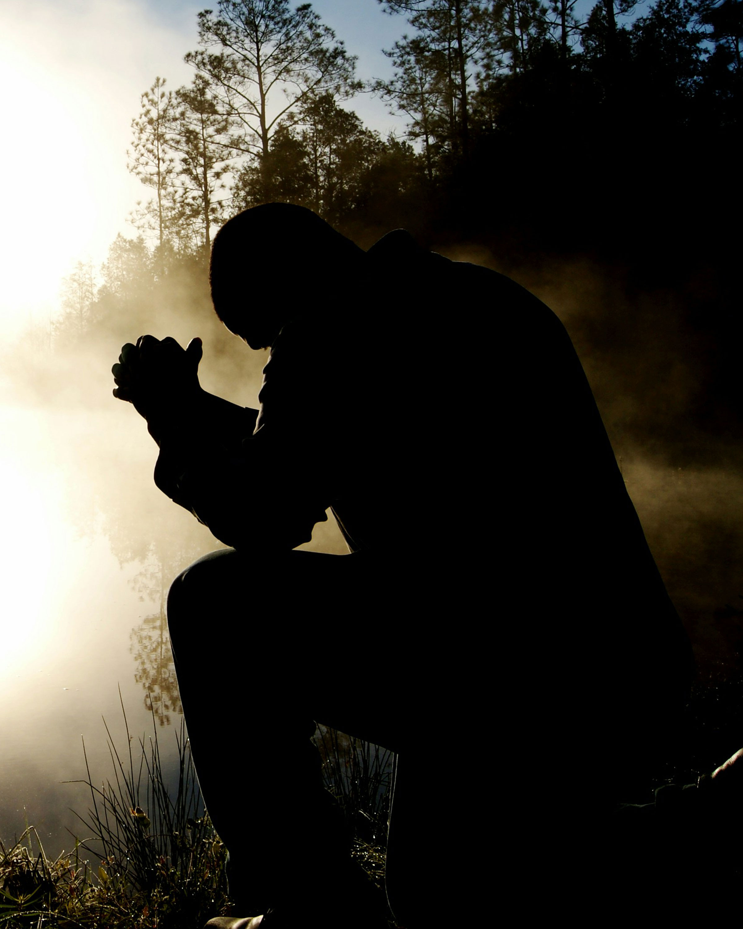 Man praying during a misty sunrise.