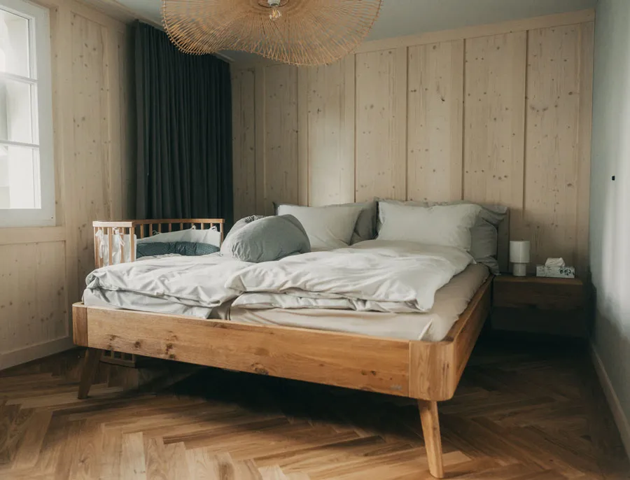 Doppelbett mit Holzrahmen und Zustellbett in holzverkleidetem Raum