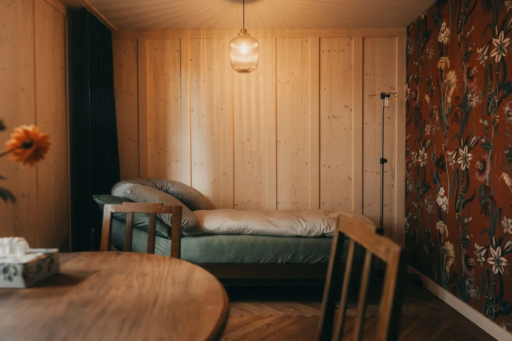 Zimmer mit Holzwänden, Blumentapete, rundem Holztisch und Bett