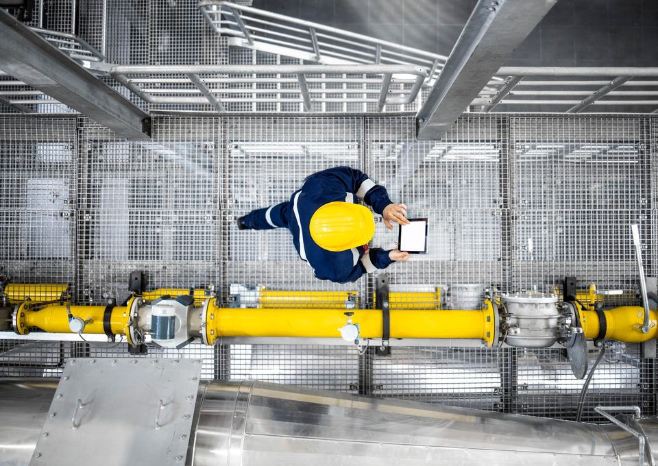 Technician with a tablet above a yellow pipeline, seen from above