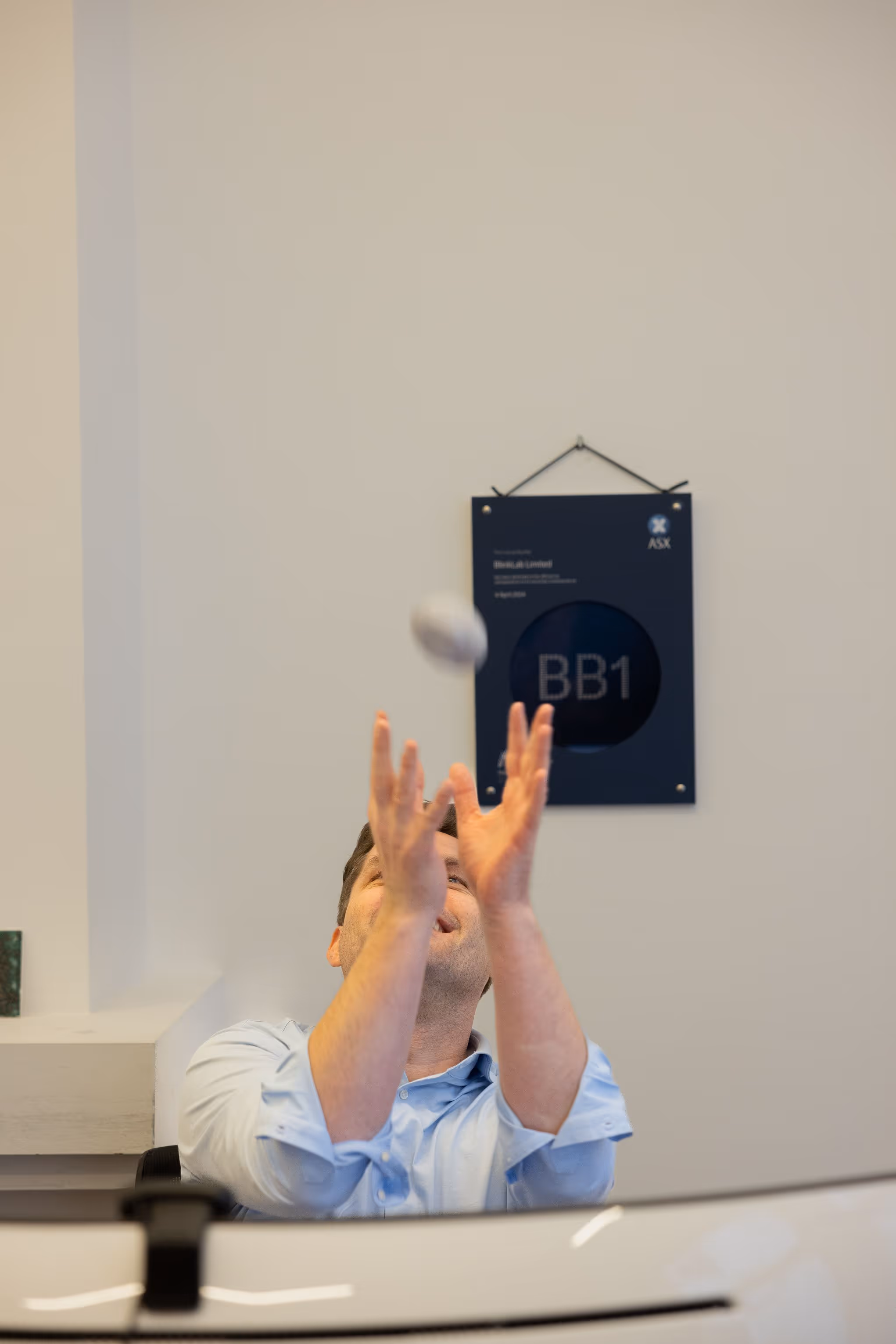 Man in a light blue shirt tossing a small round object into the air in an office setting.