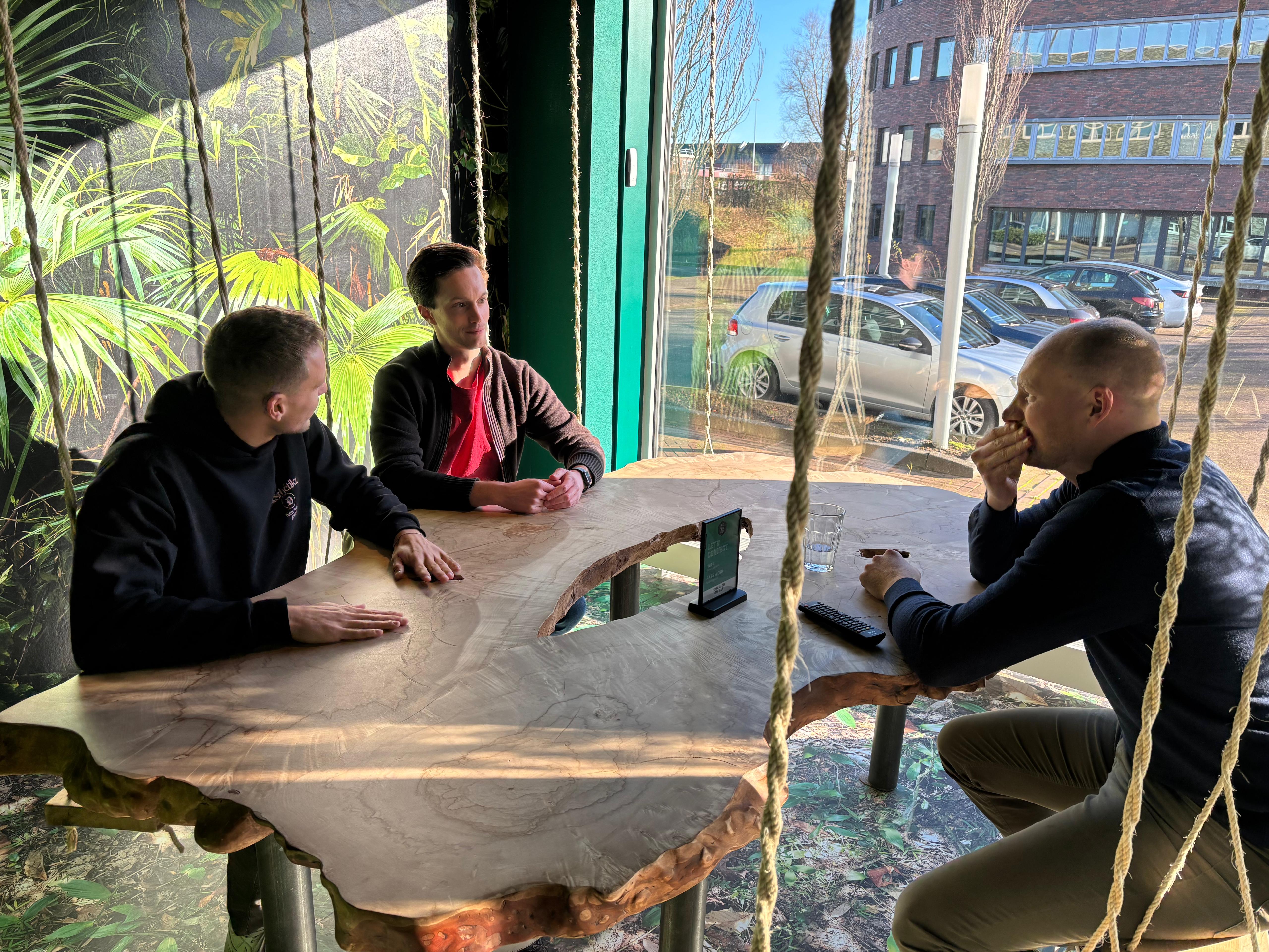 Sjoerd Beljon zit met twee Kobeon-teamleden aan een grote houten tafel in de Jungle ruimte, in overleg