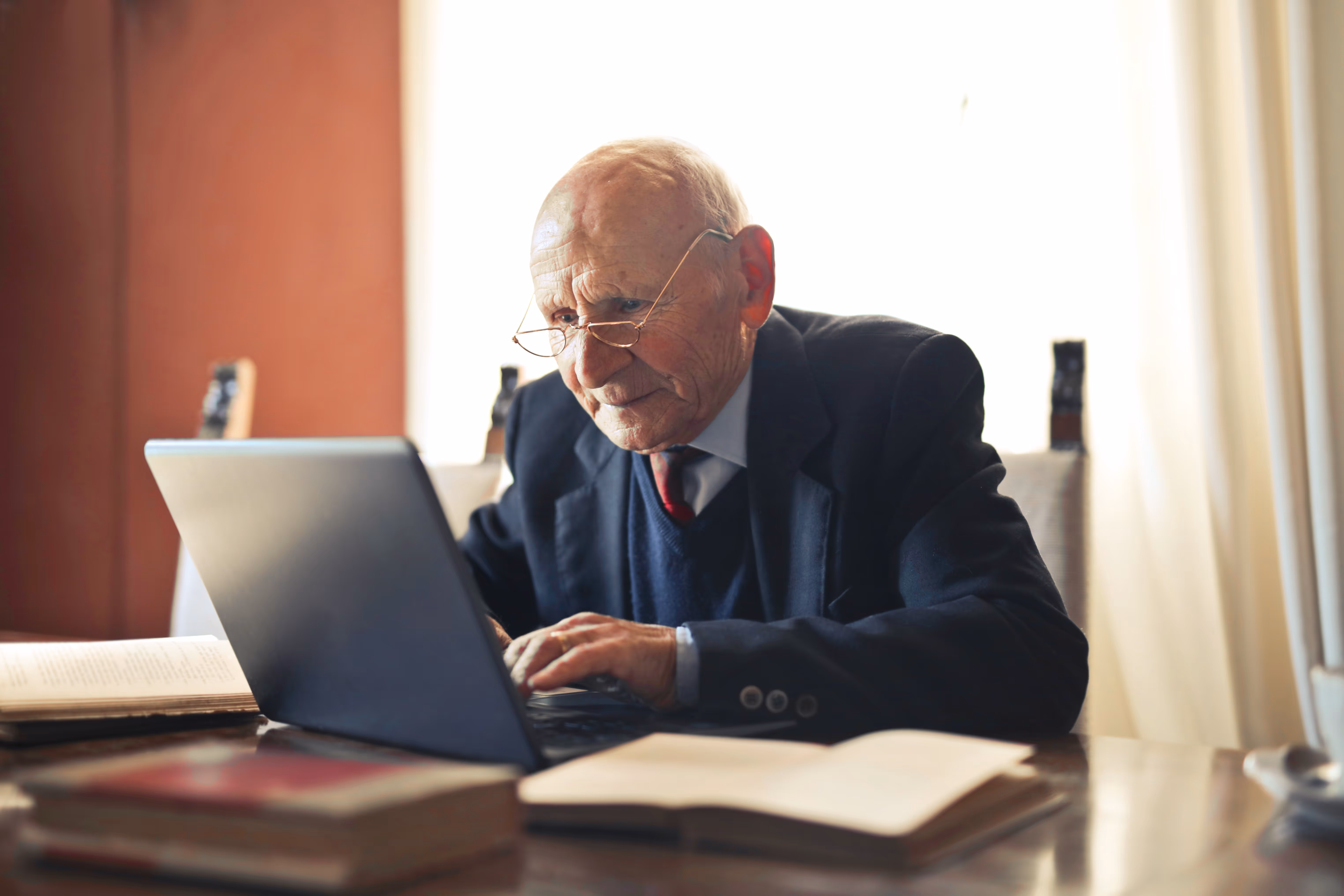 Elderly man wearing glasses uses a laptop.