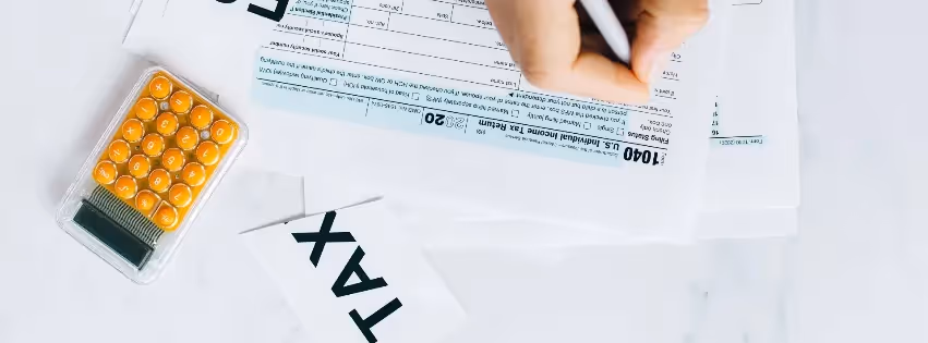 Hand filling out tax form with calculator and tax documents