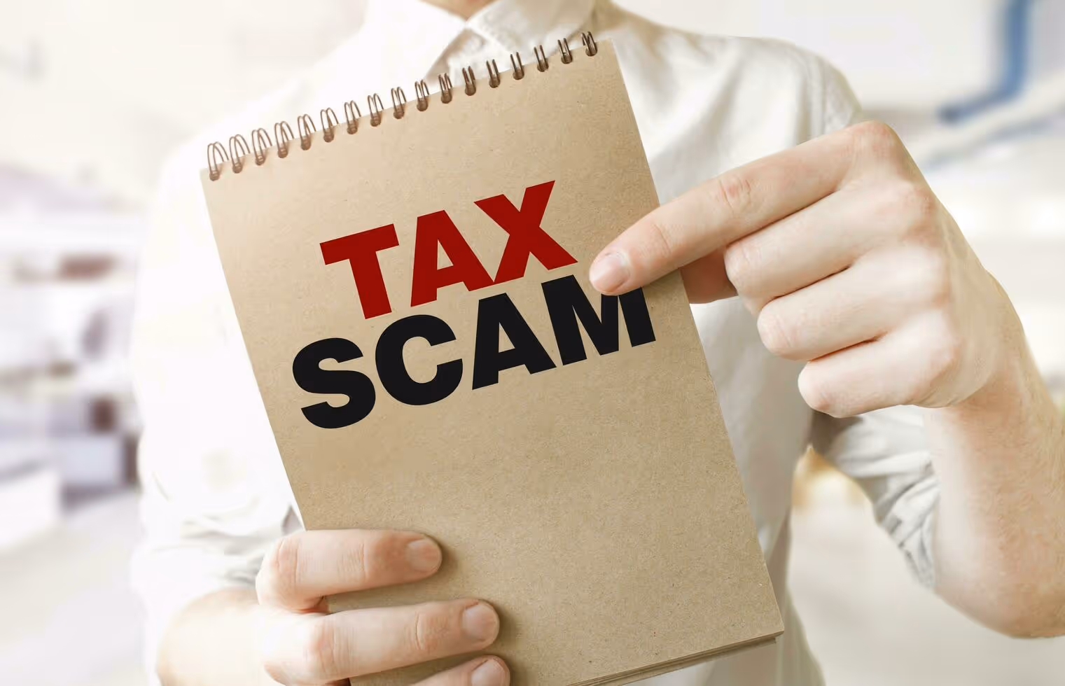 Person holding notebook with red and black text Tax Scam warning. And help with the IRS