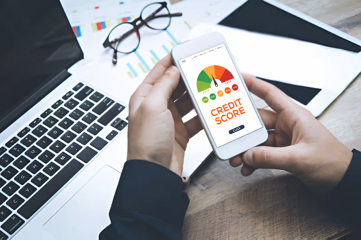 Hands holding smartphone displaying credit score meter with laptop nearby