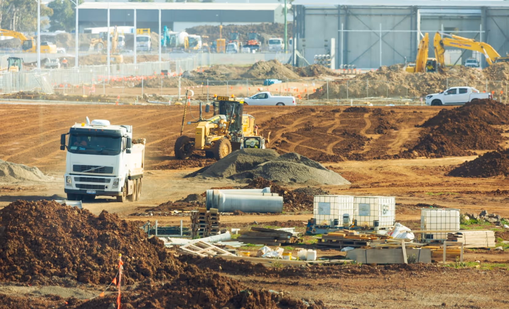 Construction site featuring dirt market operations with trucks, heavy machinery, and piles of soil and equipment.