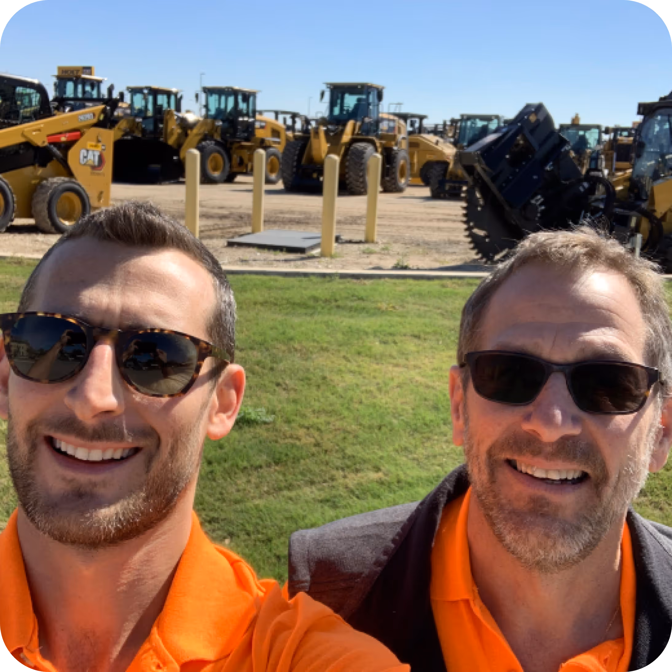 The founders of Soil Connect smiling in front of heavy construction equipment at a company equipment yard on a sunny day.