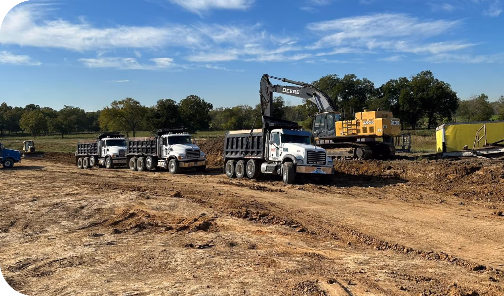 Dirt market construction site with dump trucks lined up and an excavator loading soil under a clear sky.