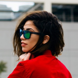 Woman with dark wavy hair wearing sunglasses and a red shirt looking to the side.