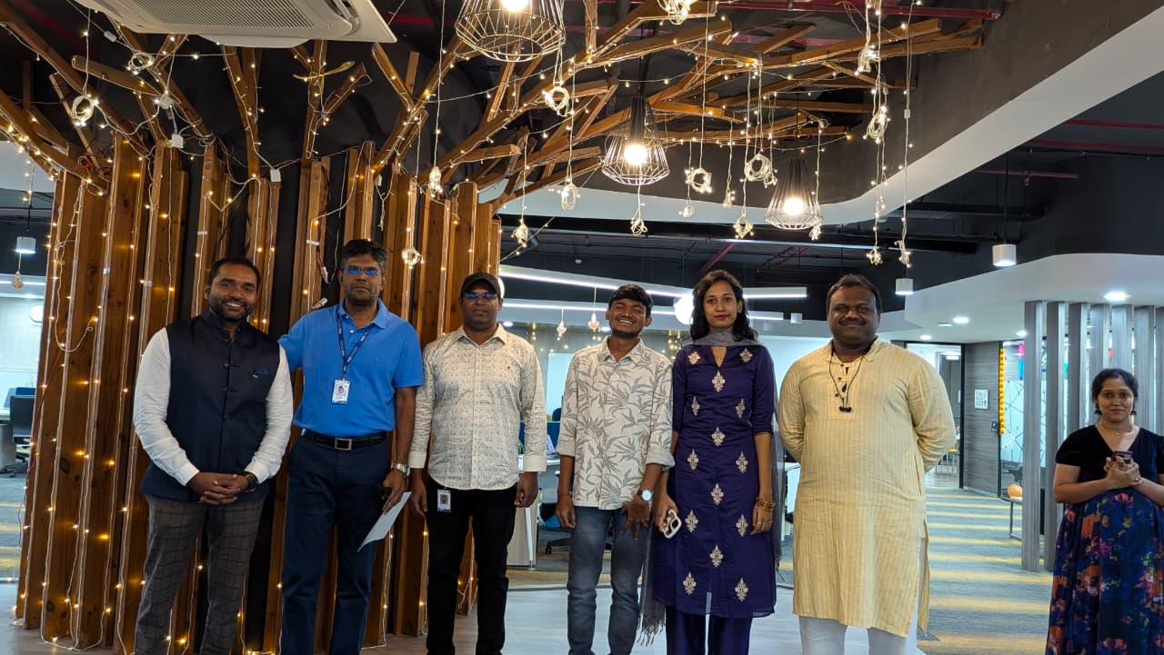 Seven people standing indoors in front of a decorative wooden structure with string lights, smiling and posing for the photo.