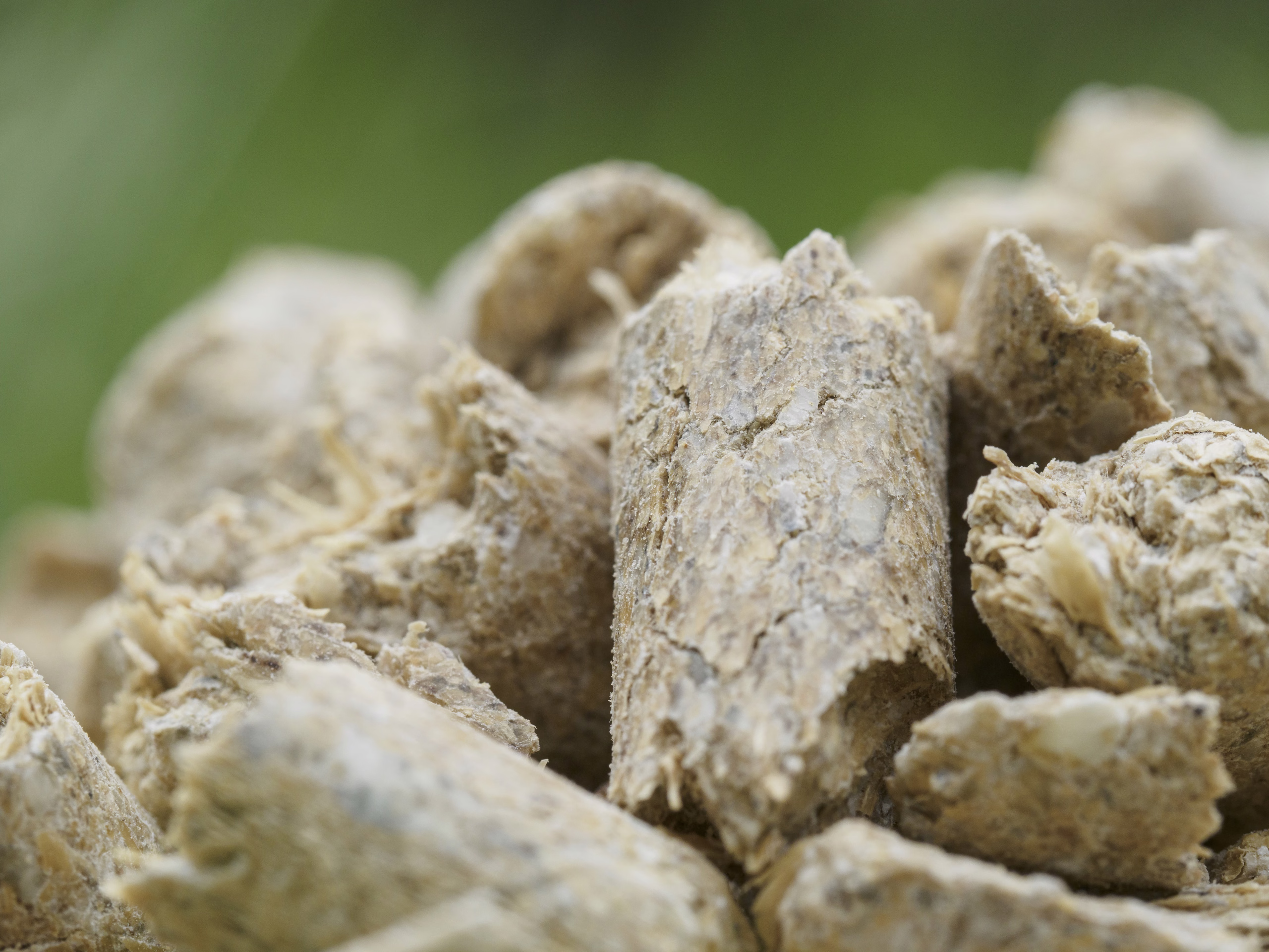 Close-up of rough-textured, cylindrical wood pellets clustered together against a blurred green background.