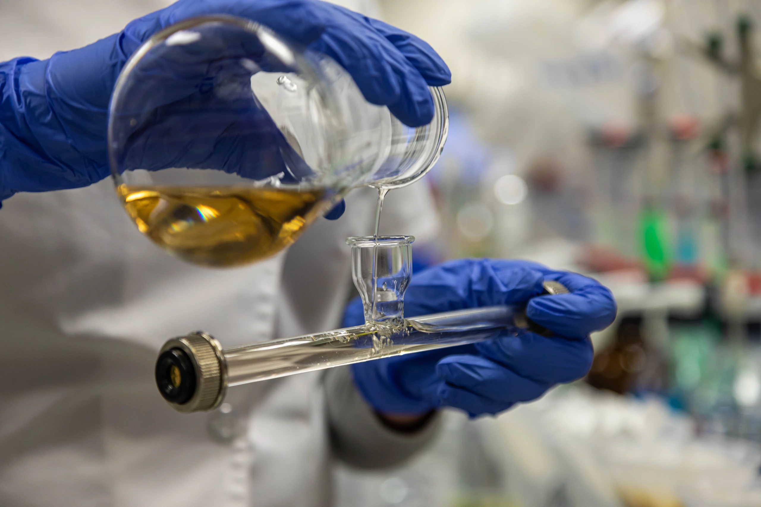 Lab technician in blue gloves pouring a sample into a measuring tube