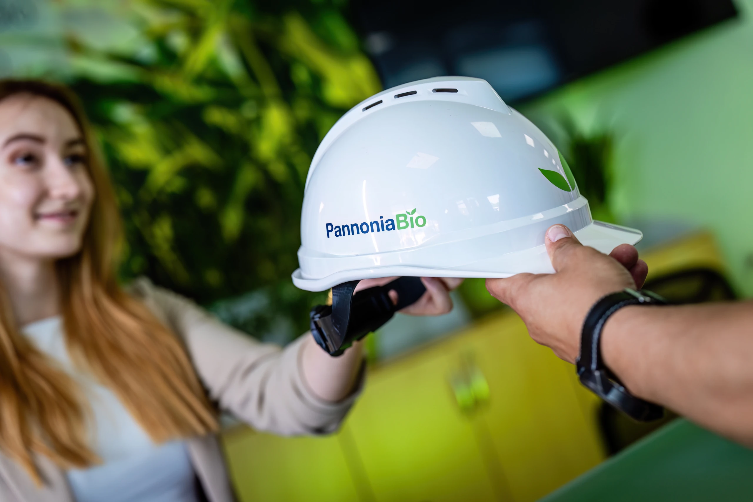 A Pannonia Bio hard hat being handed to a smiling new colleague