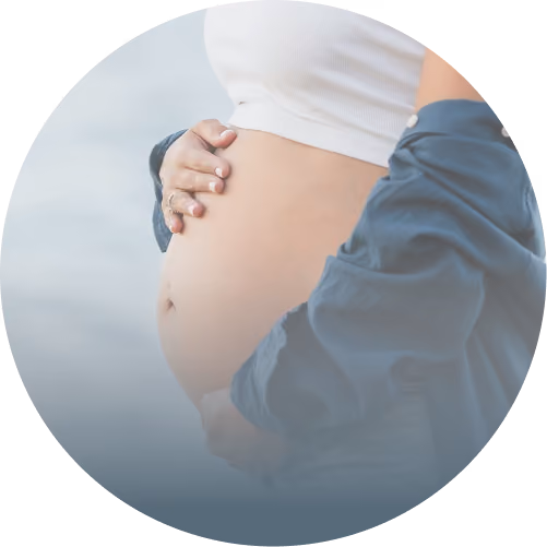 Close-up of a pregnant belly with two hands gently cradling it, one from behind wearing a blue sleeve.