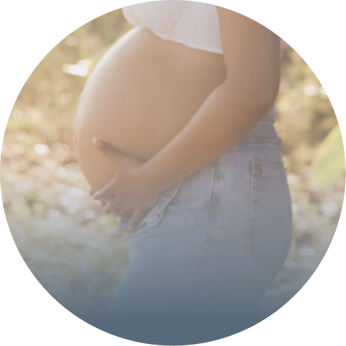 Side view of a pregnant woman gently holding her bare belly outdoors with soft natural light.