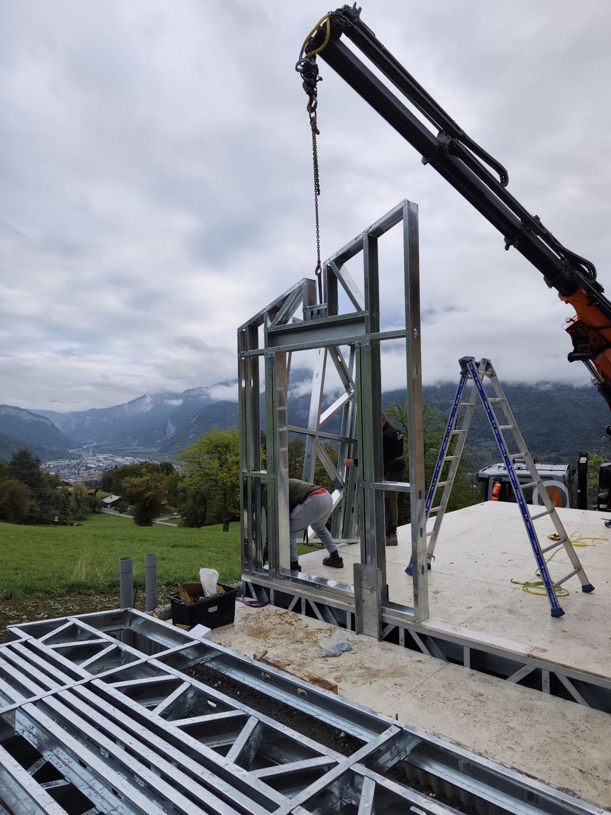 Pose à la grue d'un mur en ossature métallique légère sur le plancher de la surélévation, vallée en fond