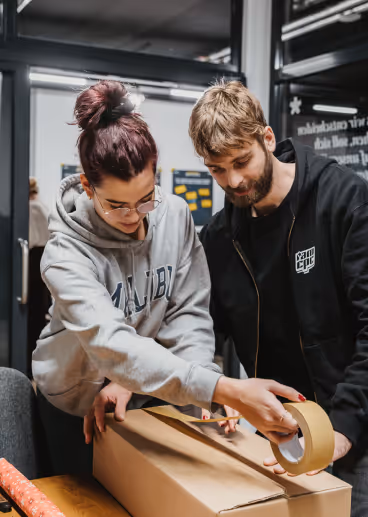 Zukleben eines Spendenkartons durch zwei Personen.