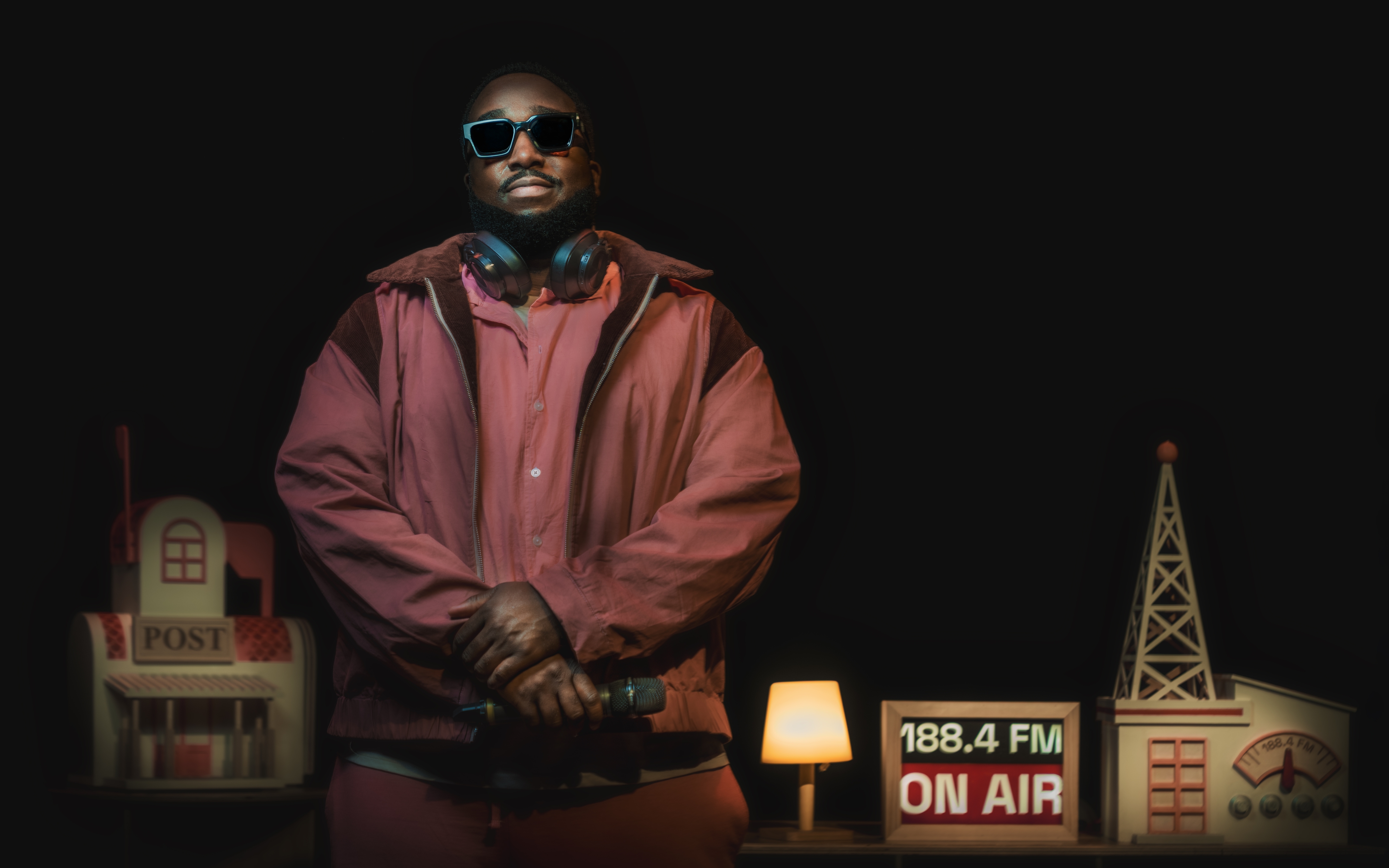 A DJ holding a microphone and smiling behind a table with a sign '188.4FM ON AIR'