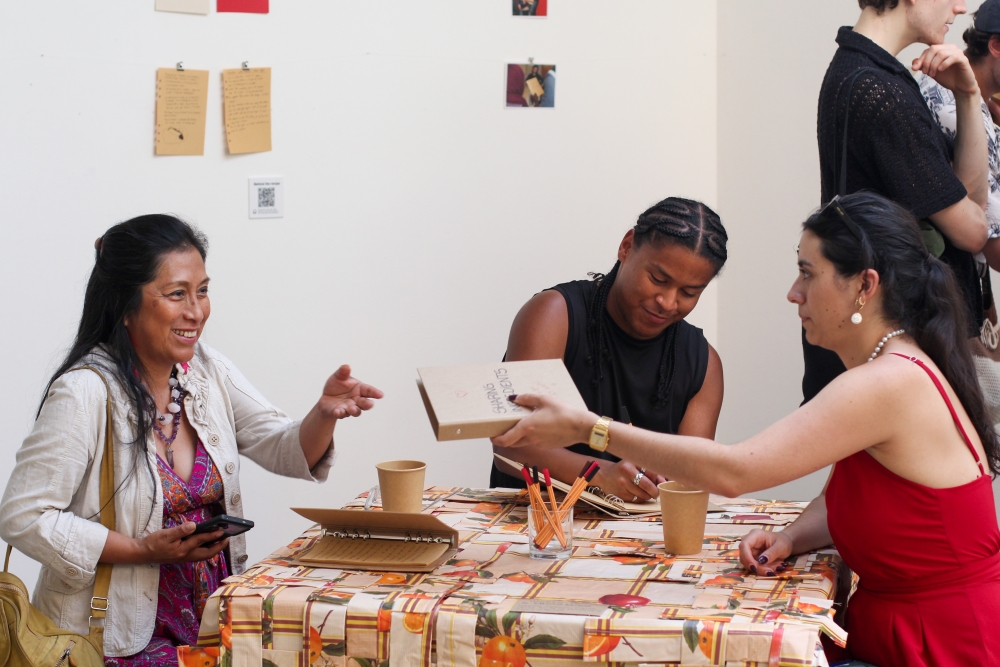 Audience members writing notes on a kitchen table in an exhibition space