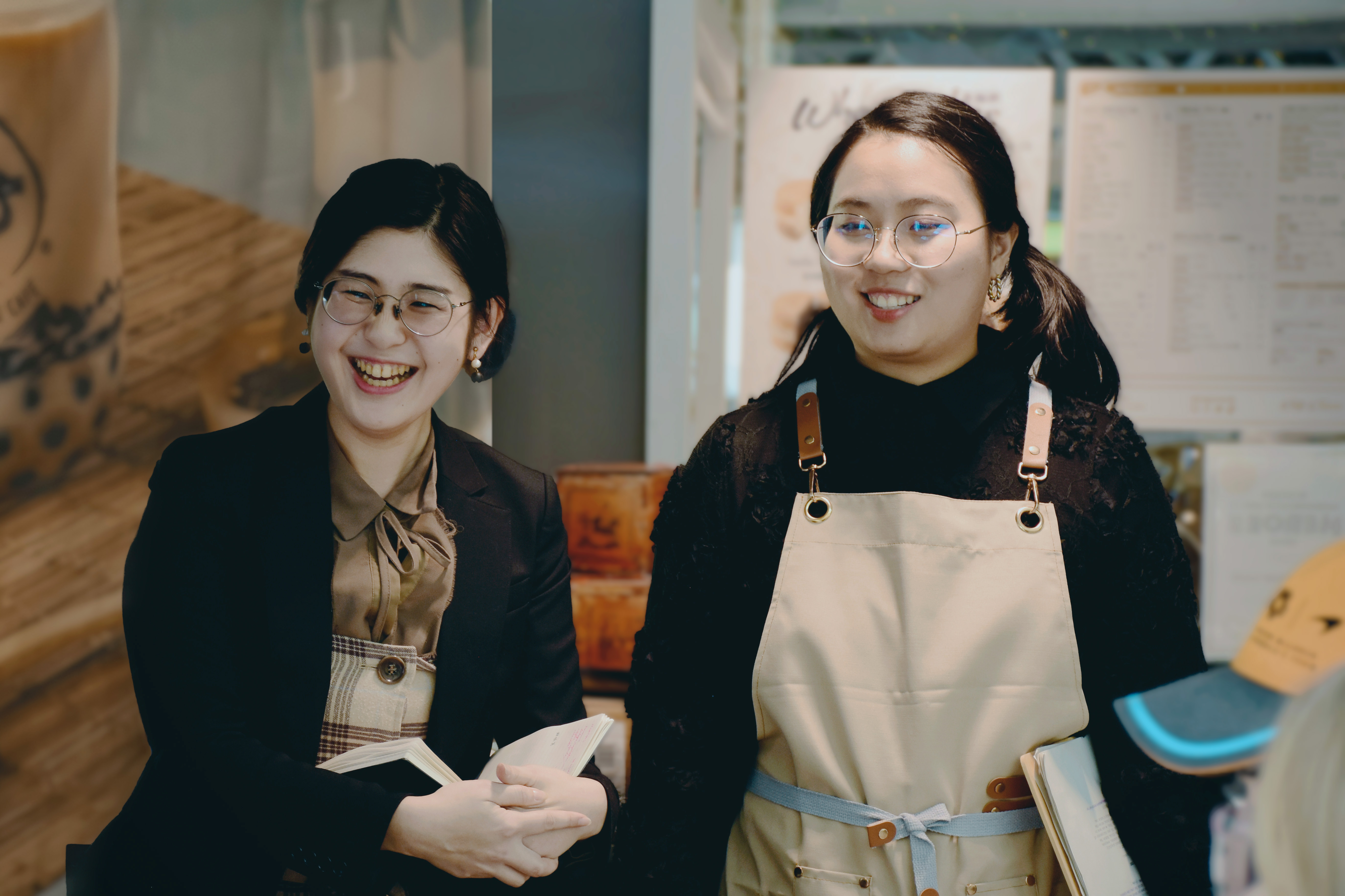 Two East Asian women wearing black and beige outfits, smiling