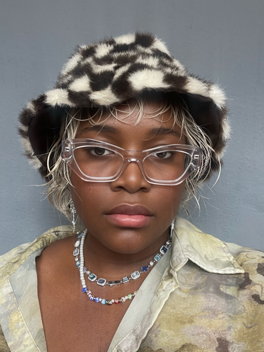 Black woman wearing a black and white furry hat and glasses staring at the camera
