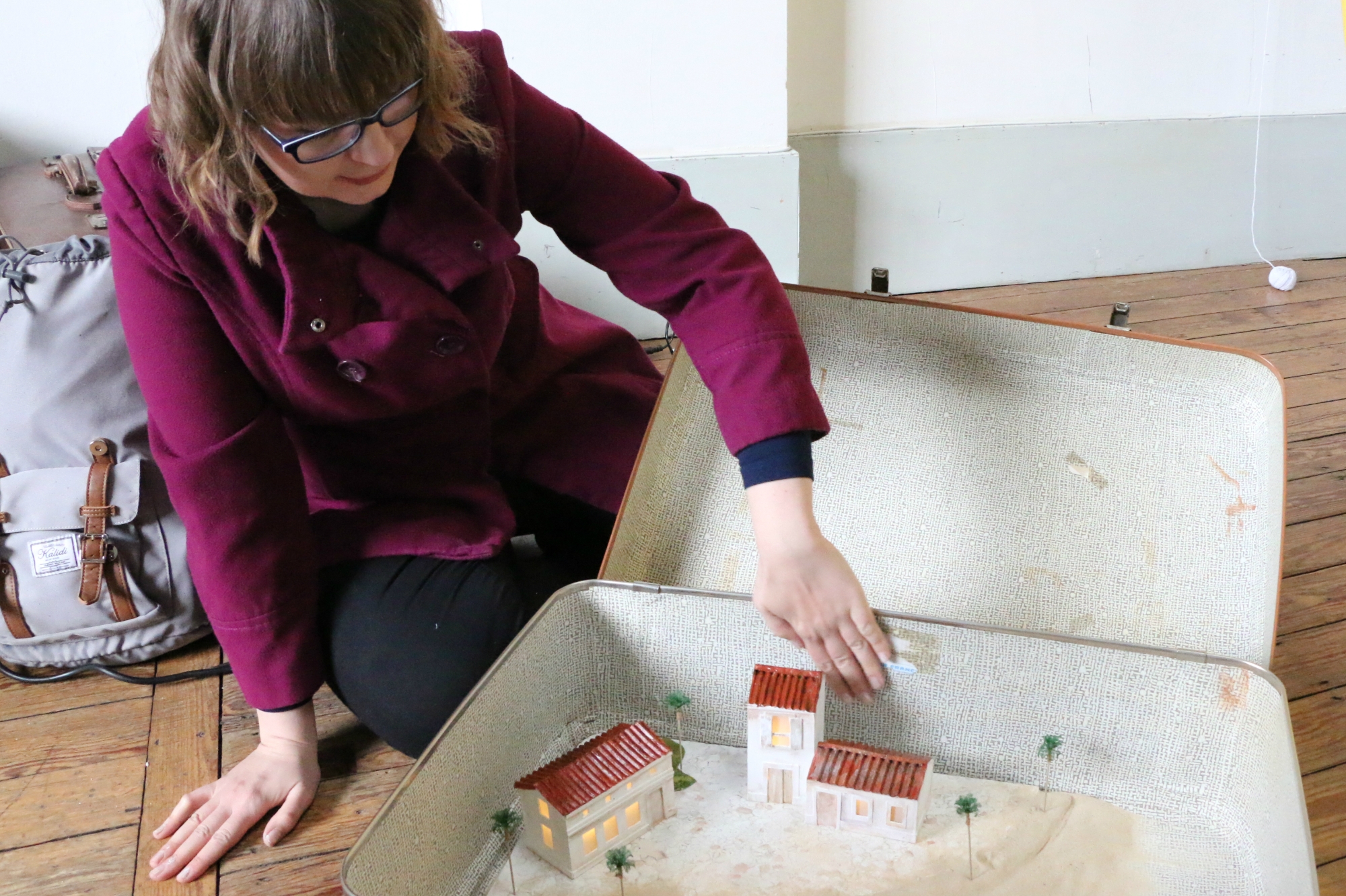 Miniature houses lit from within inside a suitcase, with an audience member leaning over them