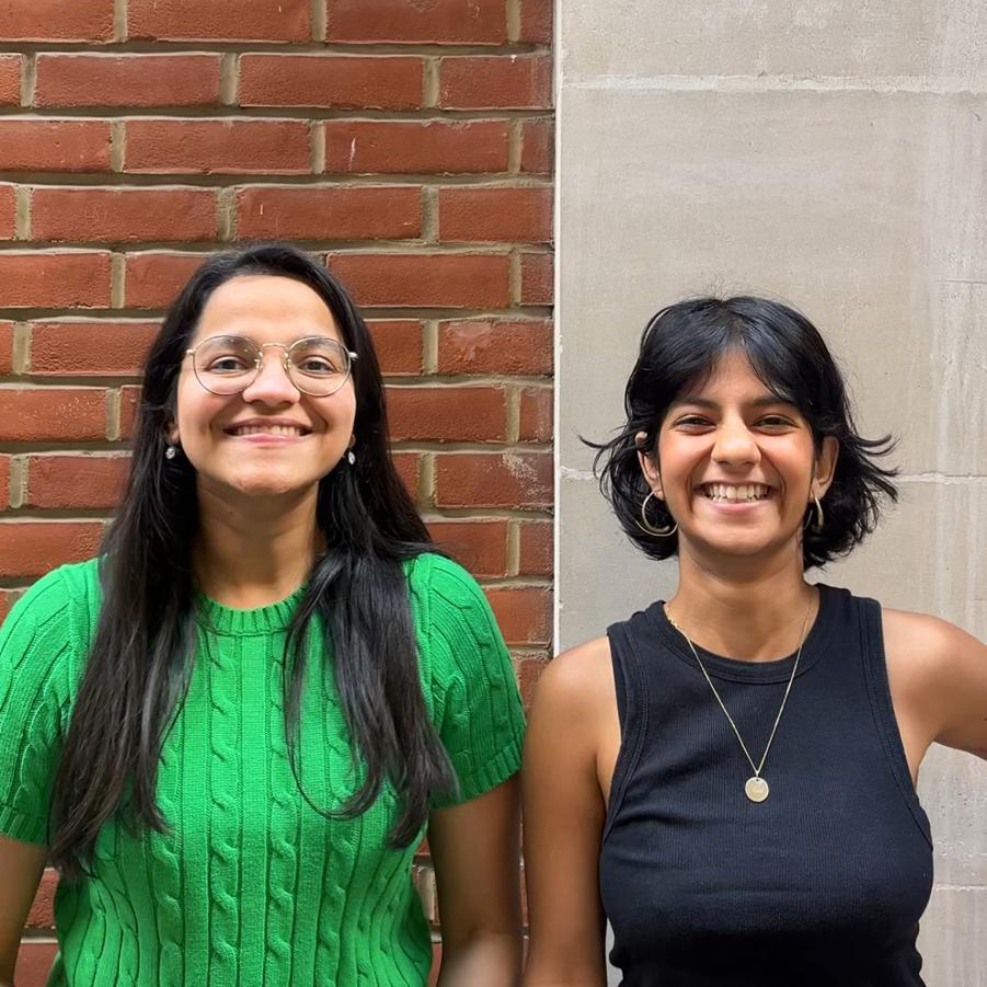 Two South Asian woman smiling at the camera in an outdoor location
