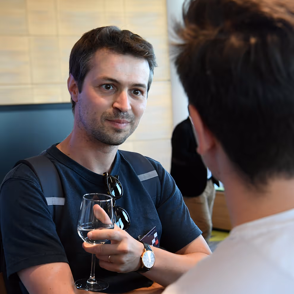 Man holding a wine glass engaged in conversation with another person in a casual indoor setting.